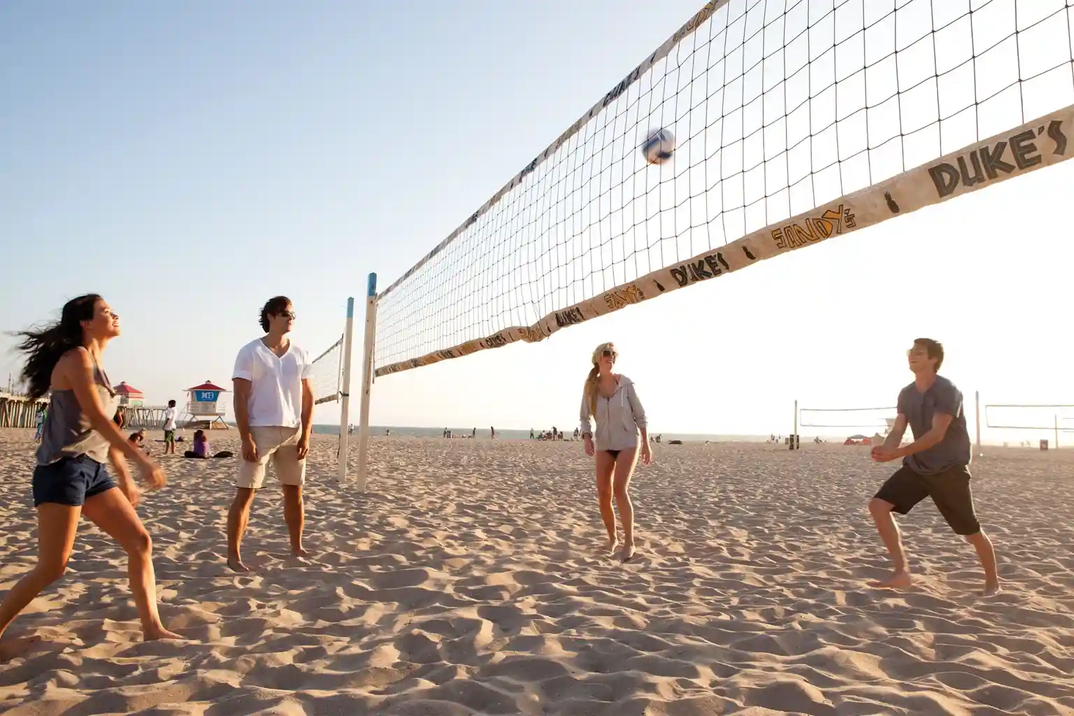 Group of friends playing beach volleyball on a sandy Kerala beach during sunset with ocean in the background