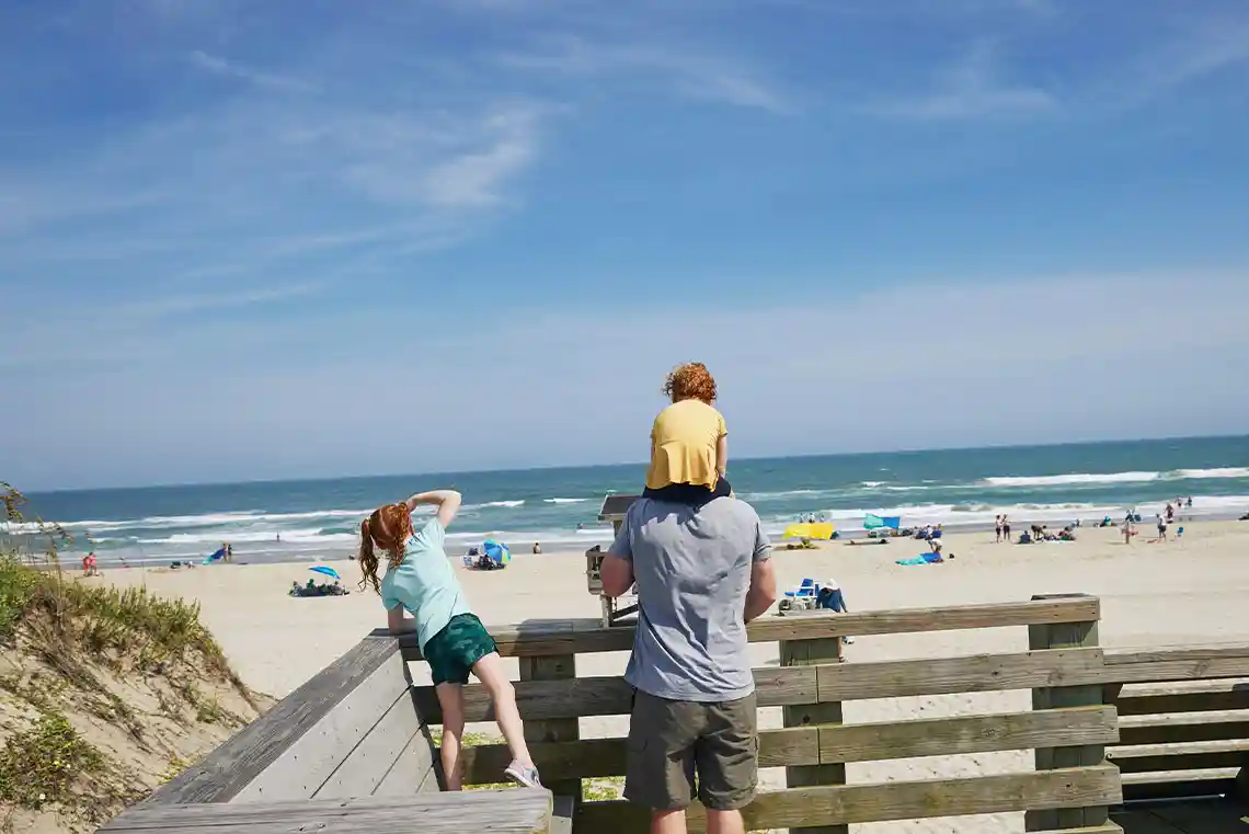 Family looking out over the ocean from a Corolla beach overlook with wide sandy shoreline and blue Outer Banks water