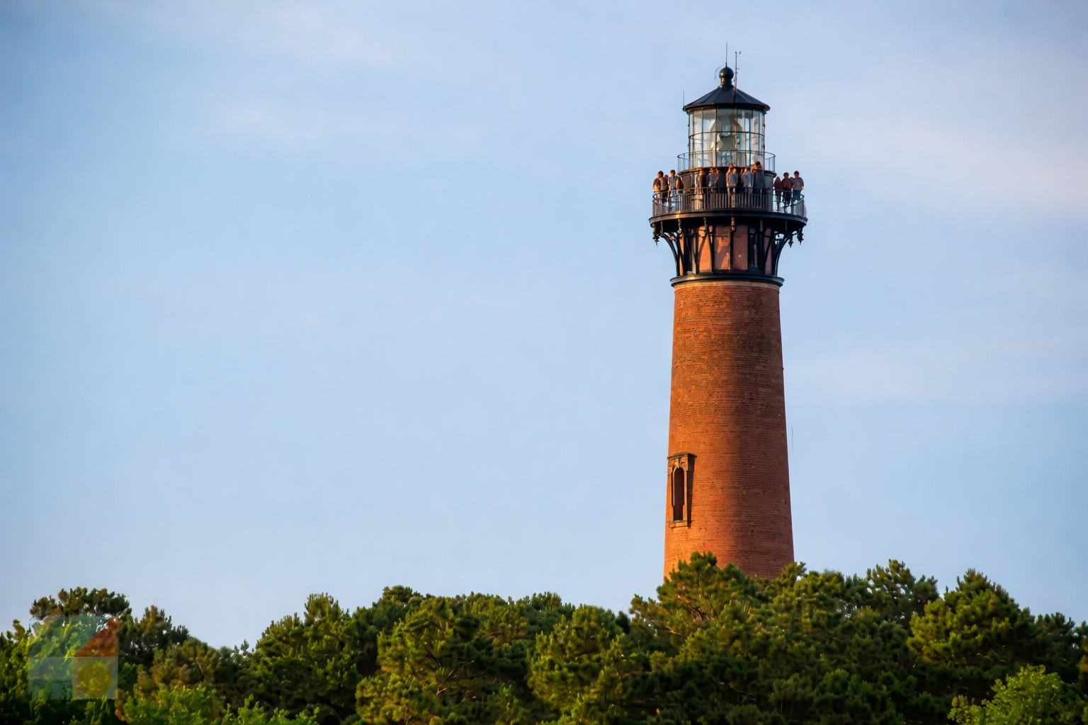 Currituck Beach Lighthouse rising above maritime forest in Historic Corolla Park, Outer Banks North Carolina, with visitors enjoying panoramic views at sunset