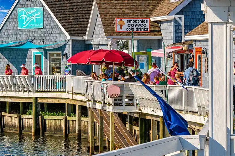Scenic Duck, North Carolina boardwalk along the waterfront with shops, outdoor dining, and people enjoying a sunny day in the Outer Banks.