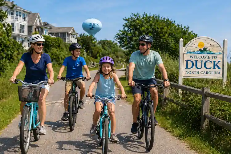 Family riding bikes along a scenic path in Duck, North Carolina with coastal homes and greenery, enjoying a sunny day in the Outer Banks.