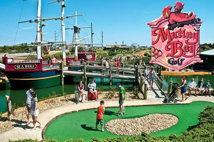 Families playing mini golf at Mutiny Bay Adventure Golf with pirate ship and water features in Nags Head, Outer Banks, North Carolina.