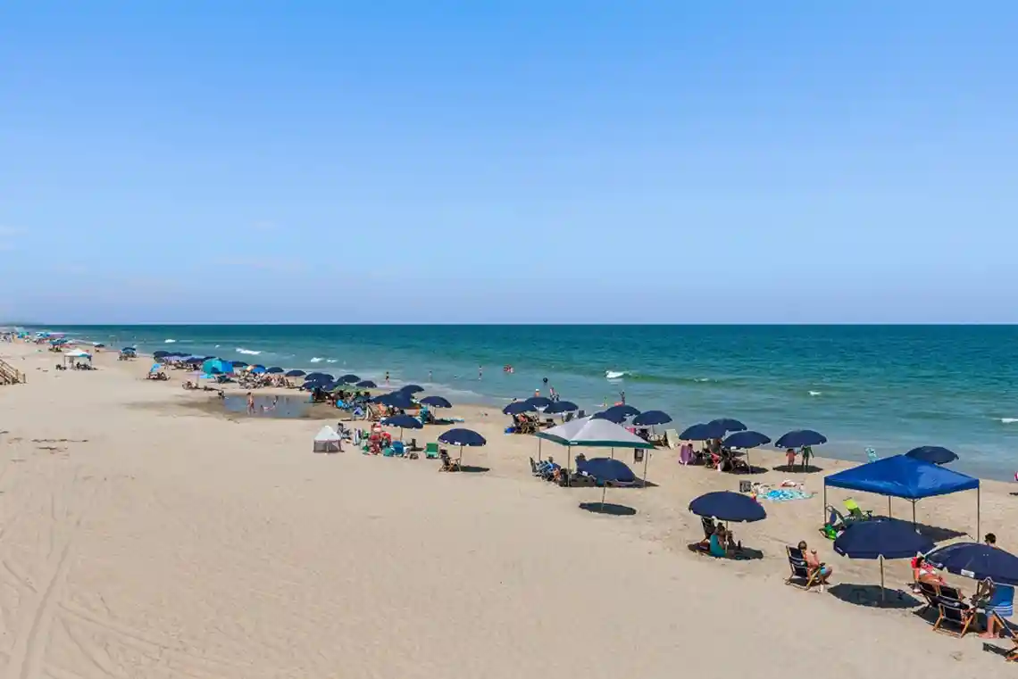 Aerial view of Corolla Outer Banks beach with umbrellas, families relaxing on the sand, and clear blue ocean water along the shoreline