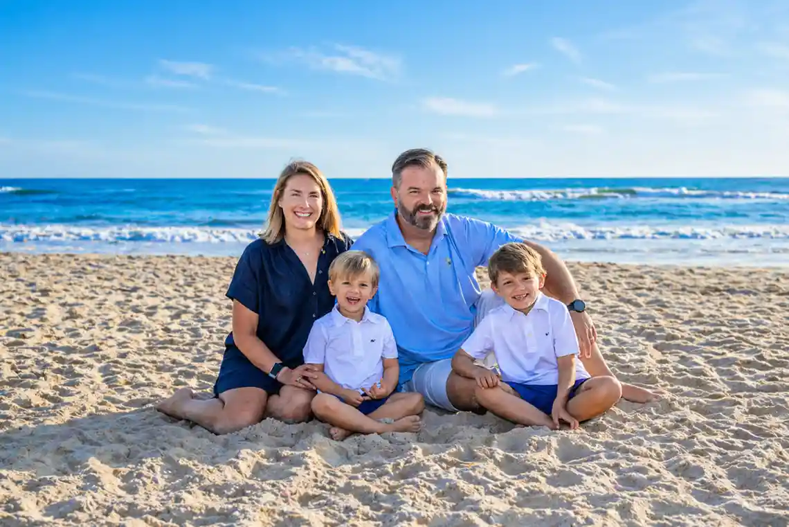 Family sitting together on the sandy beach in Corolla North Carolina with bright blue ocean waves in the background during an Outer Banks vacation