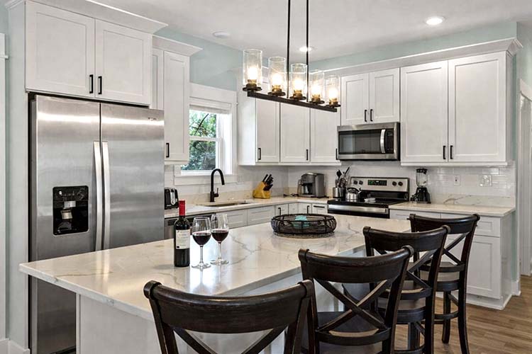 Modern kitchen at Sonoma's Hideaway in Corolla NC with stainless steel appliances, large island seating, wine glasses, and fully equipped layout