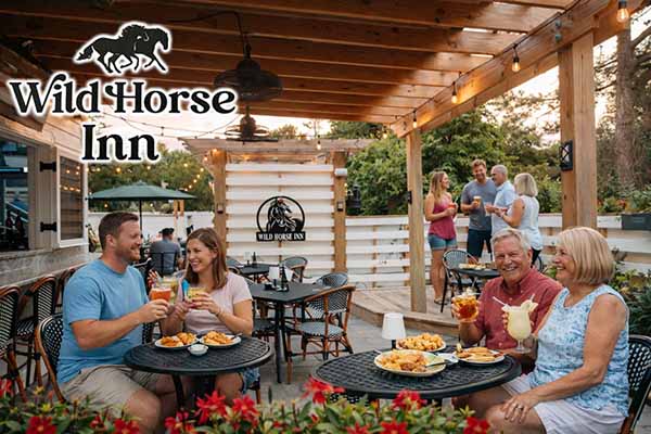 Guests enjoying drinks and appetizers on the outdoor patio at Wild Horse Inn in Historic Corolla Village, Outer Banks, with string lights, wooden pergola, and a relaxed coastal dining atmosphere.