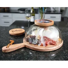 Glass smoking cloche dome with round wooden cutting board and handle with charcuterie being smoked
