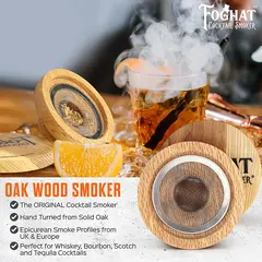 Foghat Cocktail Smoker infusing bourbon in rocks glass with visible aromatic smoke and whiskey barrel oak chips beside it.