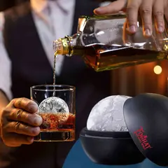 Whiskey being poured over a crystal-clear ice ball made with the Foghat ice sphere mold