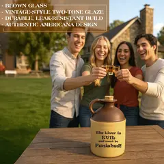 Ceramic moonshine jug with brown top, beige body, cork stopper, and printed text ‘The liver is evil and must be punished,’ displayed on an outdoor wooden table with people holding shot glasses in the background