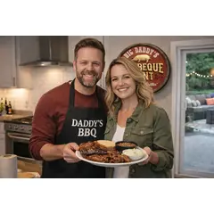 Couple holding BBQ platter in kitchen with personalized barrel end barbecue sign on wall
