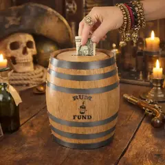 Mini oak barrel piggy bank with engraved Rum Fund graphic on rustic pirate bar table with skull decor and rum bottle