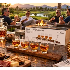 Thousand Oaks Barrel Co. Whiskey Stave Flight Set featuring four Glencairn whiskey tasting glasses filled with bourbon, a solid American oak stave display, and glass pourer. Displayed on an outdoor patio at sunset with gift packaging, while friends enjoy whiskey around a fire pit overlooking a scenic golf course.