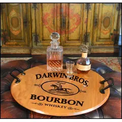'Darwin Bros.' 21-inch round authentic oak barrel head serving tray with wrought iron handles displaying bourbon decanter and glasses in a rustic bar setting.
