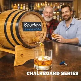 Chalkboard Series oak whiskey aging barrel with black steel hoops and writable front label pouring bourbon into a glass on a home bar
