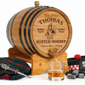 Mini oak Scotch whisky barrel with engraved Scottish bagpiper design displayed with tartan fabric and traditional accessories.