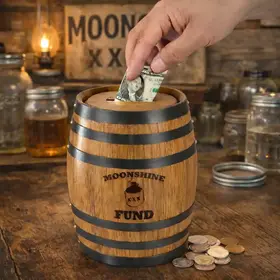 Moonshine Fund mini oak barrel piggy bank with hand placing a dollar bill into the wooden barrel savings bank on a rustic moonshine themed bar with coins.