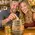 Couple dropping a coin into a mini oak barrel whiskey fund piggy bank while enjoying whiskey drinks at a bar