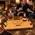 Personalized solid oak whiskey serving tray with custom name, whiskey engraving, and black wrought iron handles on a rustic coffee table, with a couple enjoying bourbon beside a cozy fireplace.