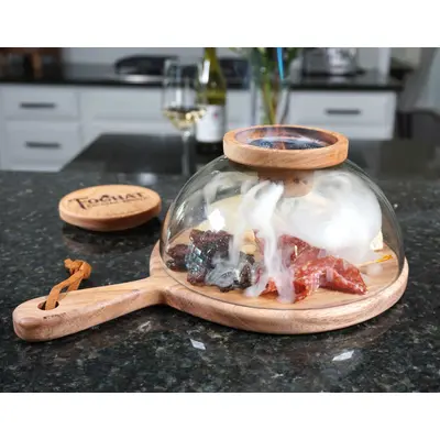 Glass smoking cloche dome with round wooden cutting board and handle with charcuterie being smoked
