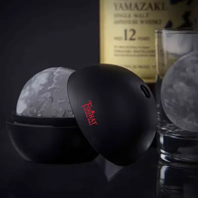 Foghat ice ball mold creating a large whiskey ice sphere beside a glass of bourbon