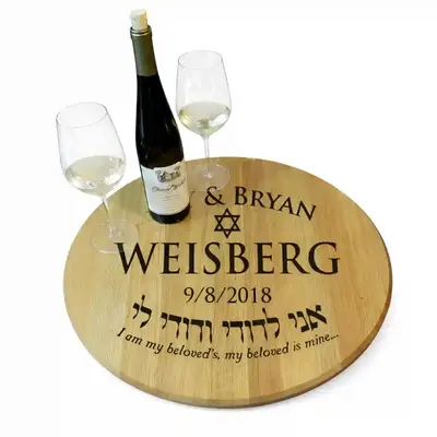 Custom engraved wine barrel head with Amy & Bryan Weisberg, Star of David, wedding date and Hebrew quote, styled with wine glasses and bottle on white background.