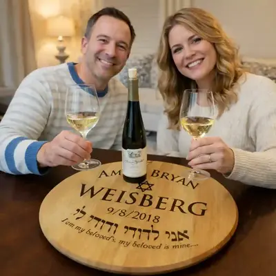 Couple enjoying wine at a table featuring a personalized engraved wine barrel head tray reading Amy & Bryan Weisberg with Jewish wedding inscription.