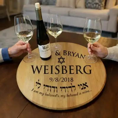 Personalized wine barrel head tray engraved with Amy & Bryan Weisberg, featuring a Star of David and Hebrew inscription, displayed on a table with wine glasses and bottle.