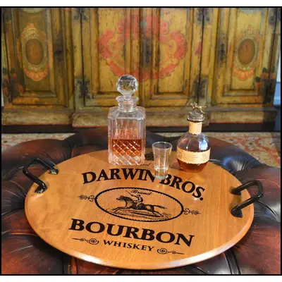 'Darwin Bros.' 21-inch round authentic oak barrel head serving tray with wrought iron handles displaying bourbon decanter and glasses in a rustic bar setting.