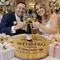Bride and groom toasting with wine glasses over a personalized wine barrel head lazy susan engraved with names and wedding date, used as a Jewish wedding gift and wine serving centerpiece.