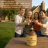 Rustic ceramic moonshine jug with vintage two-tone glaze and skull-and-crossbones design reading ‘Women or Whiskey,’ displayed on an outdoor wooden table as friends toast in the background; novelty whiskey gift and rustic home bar décor accessory.