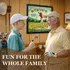 Personalized golf clubhouse dartboard cabinet set displayed in a golf-themed game room with grandfather and grandson in golf attire
