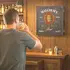 Man drinking whiskey while playing darts in a home bar featuring a personalized Bourbon Bar dartboard cabinet with custom name design, perfect for man cave or whiskey bar decor.