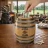Mini oak barrel Golf Fund piggy bank on a country club counter with golf clubs, tees, and change while a hand places money into the barrel savings bank.