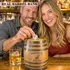 Couple dropping a coin into a mini oak barrel whiskey fund piggy bank while enjoying whiskey drinks at a bar