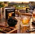 Foghat Cigar Glass and Ice Ball Mold Set featuring a crystal whiskey glass with built-in cigar holder, spherical ice mold, and gift box on a rustic outdoor table at sunset, with a luxury golf course backdrop, fire pit, and cigar accessories.